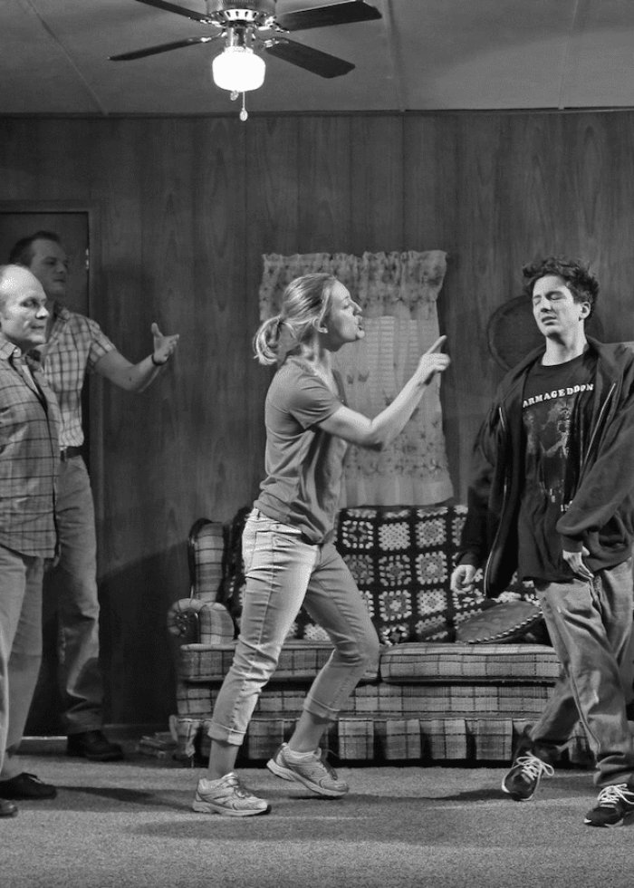 Black and white scene from a play: actors portraying a tense family drama, likely about addiction.