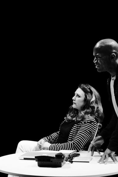 Black and white photo of a man and woman in serious discussion at a table with a phone and laptop.