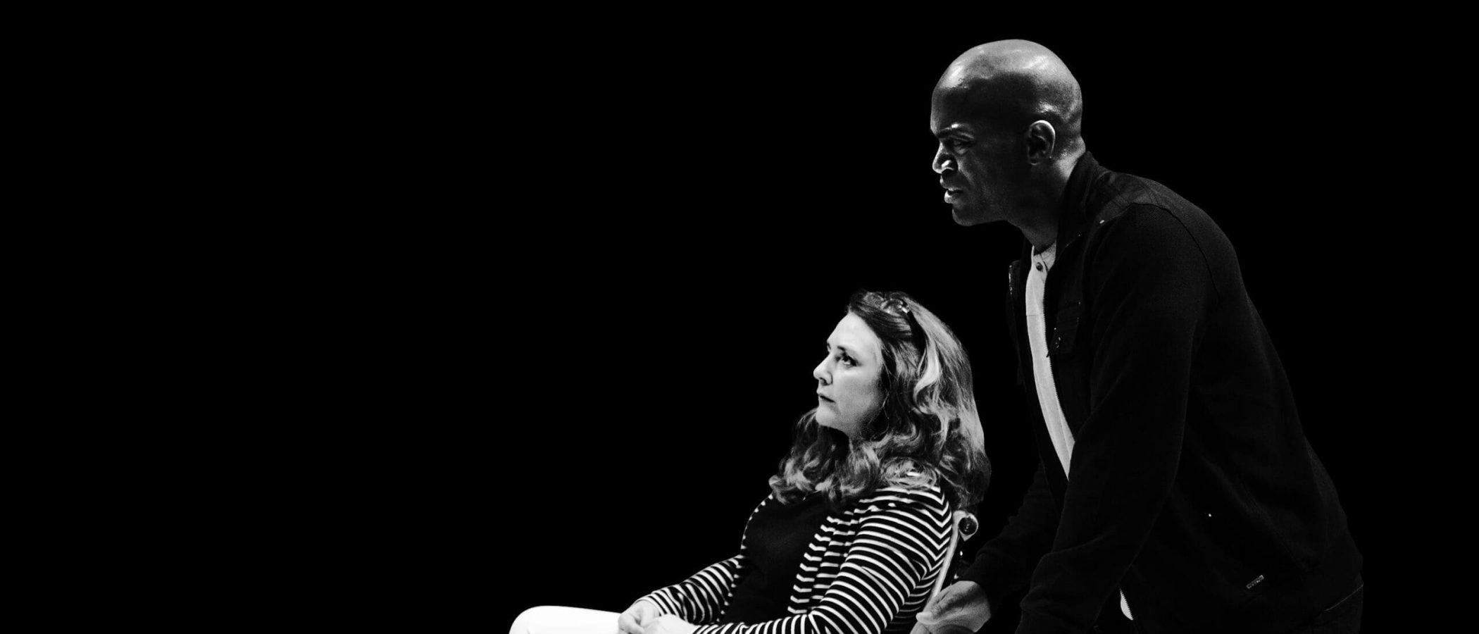 Black and white photo of a man and woman in serious discussion at a table with a phone and laptop.
