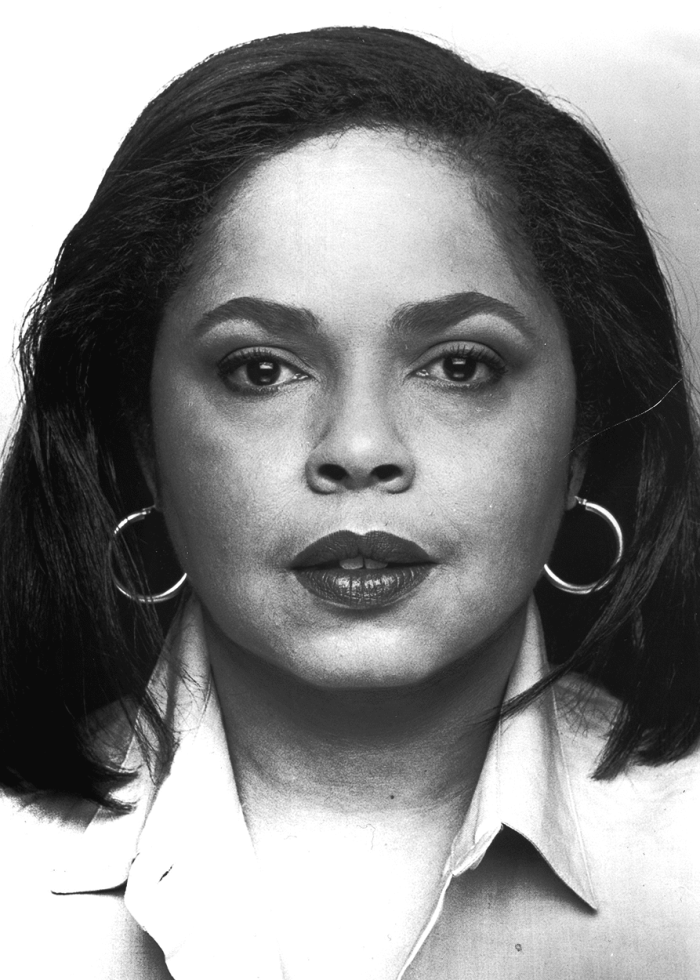 Lynda Gravatt in a close-up portrait, wearing hoop earrings and a button-down shirt.