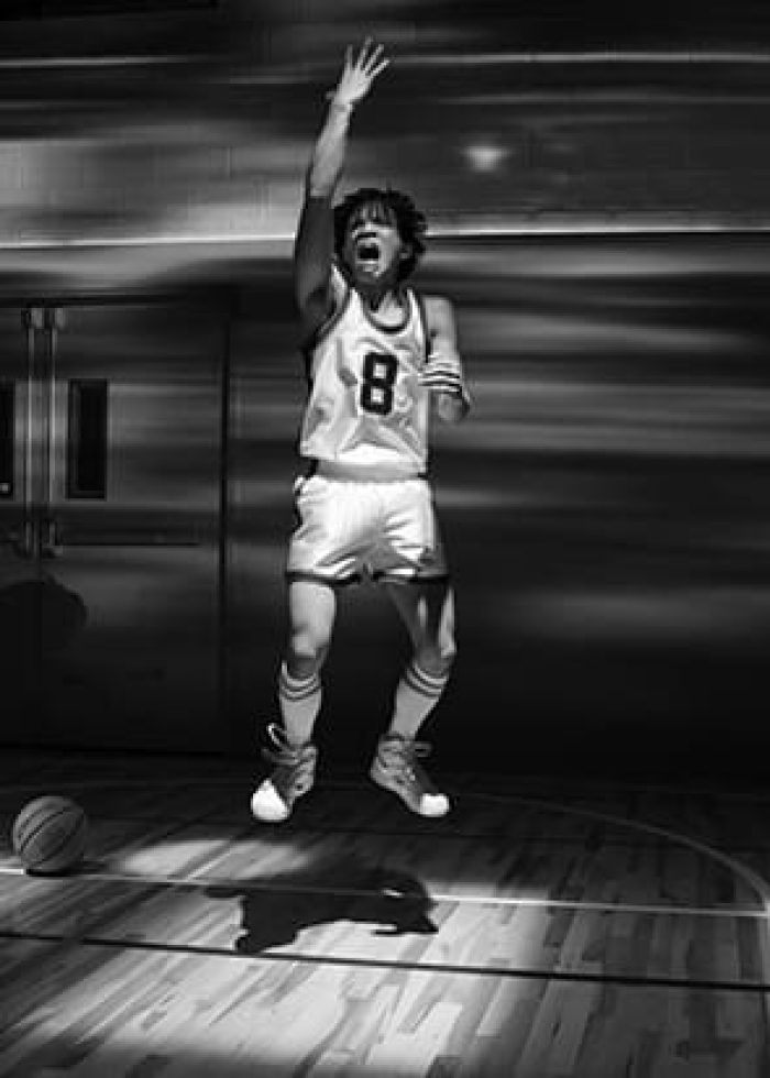 Basketball player shooting in "The Great Leap" stage play. Two men watch on a court.