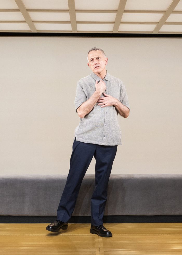 David Greenspan, standing, wearing a gray shirt and dark pants.