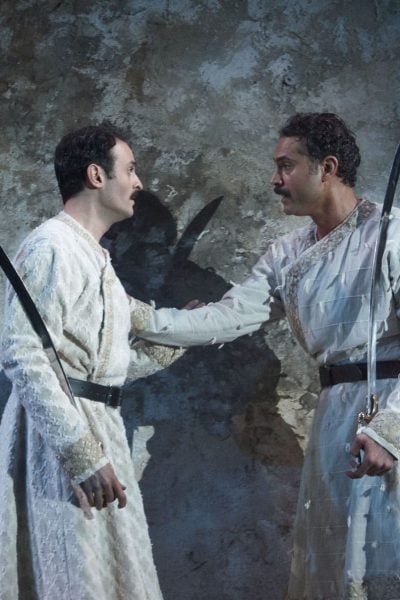 Two men in traditional white robes, holding scimitars, stand facing each other. Guards at the Taj.