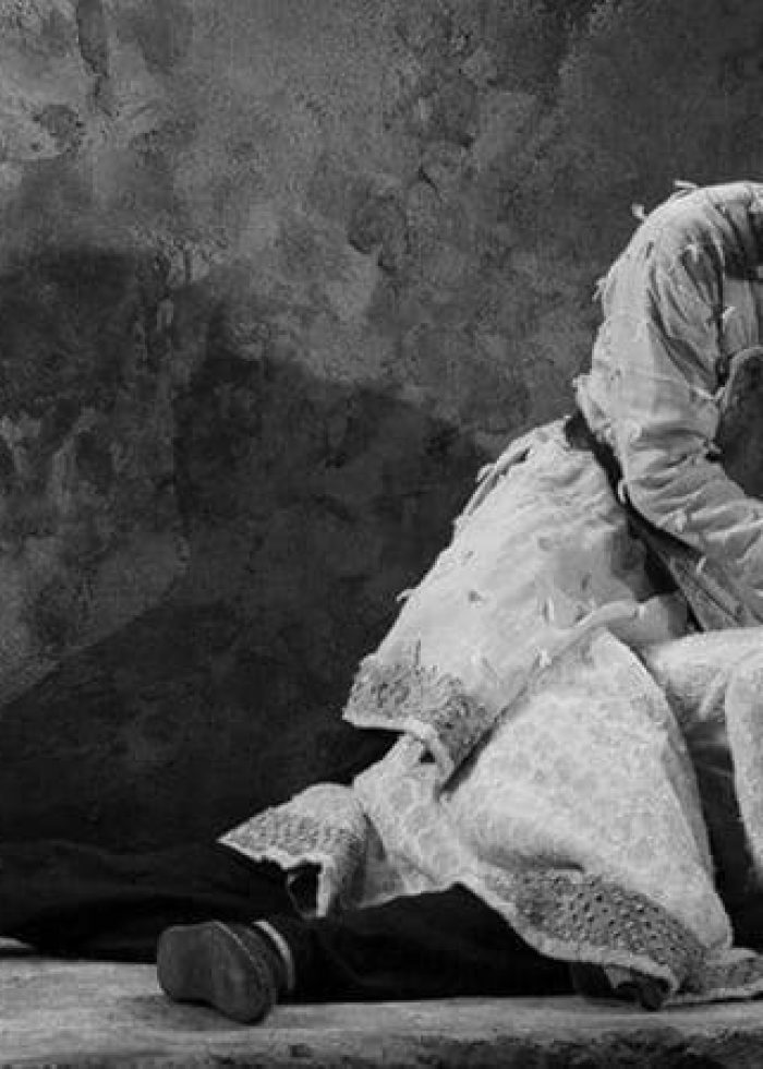 Two actors in a scene from 'Guards at the Taj', one kneeling over the other on a stage.