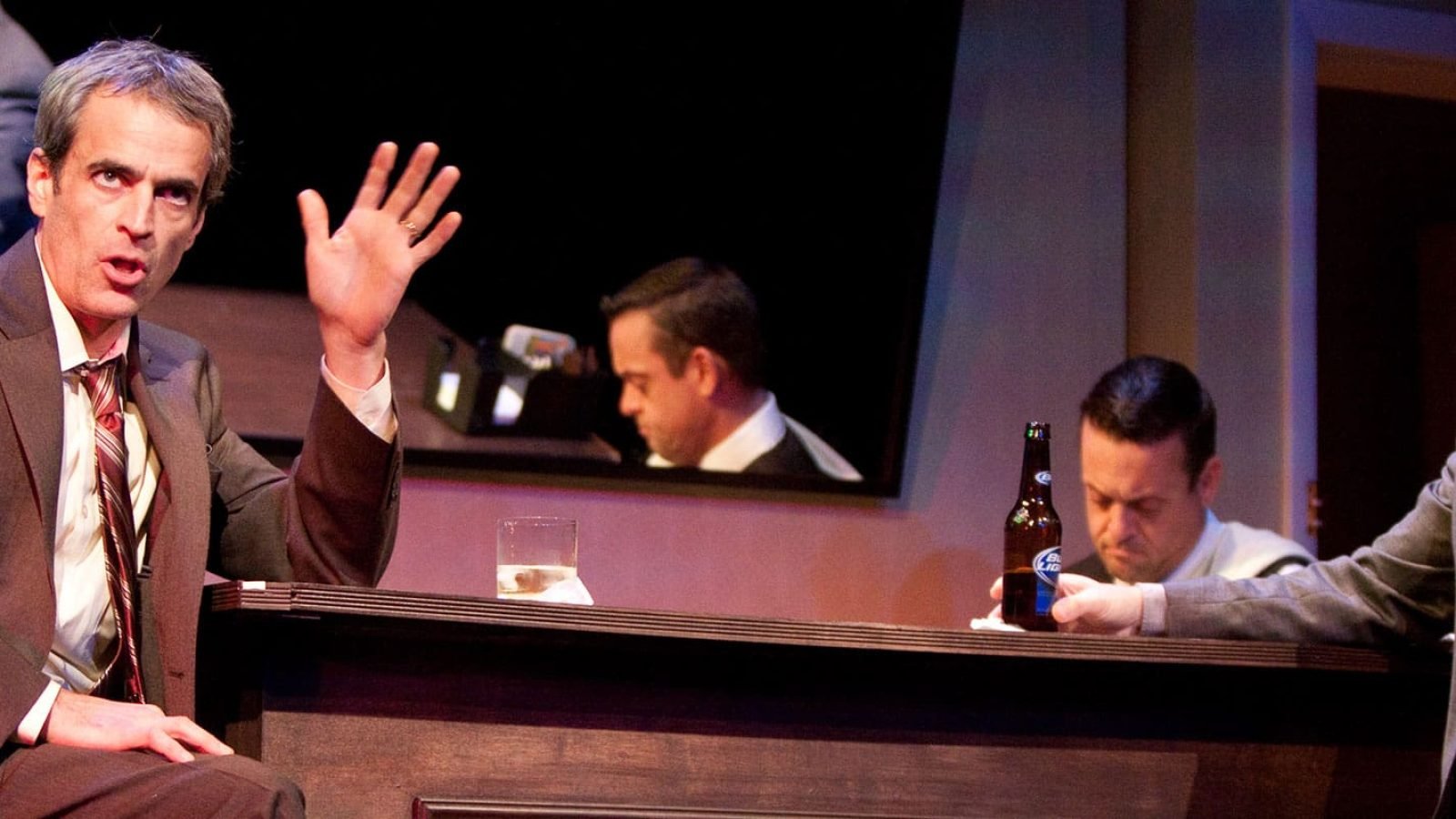 Four men in suits at a bar during happy hour, one man gestures.