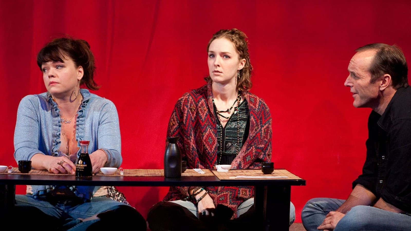 Three people enjoy happy hour at a low table with drinks.