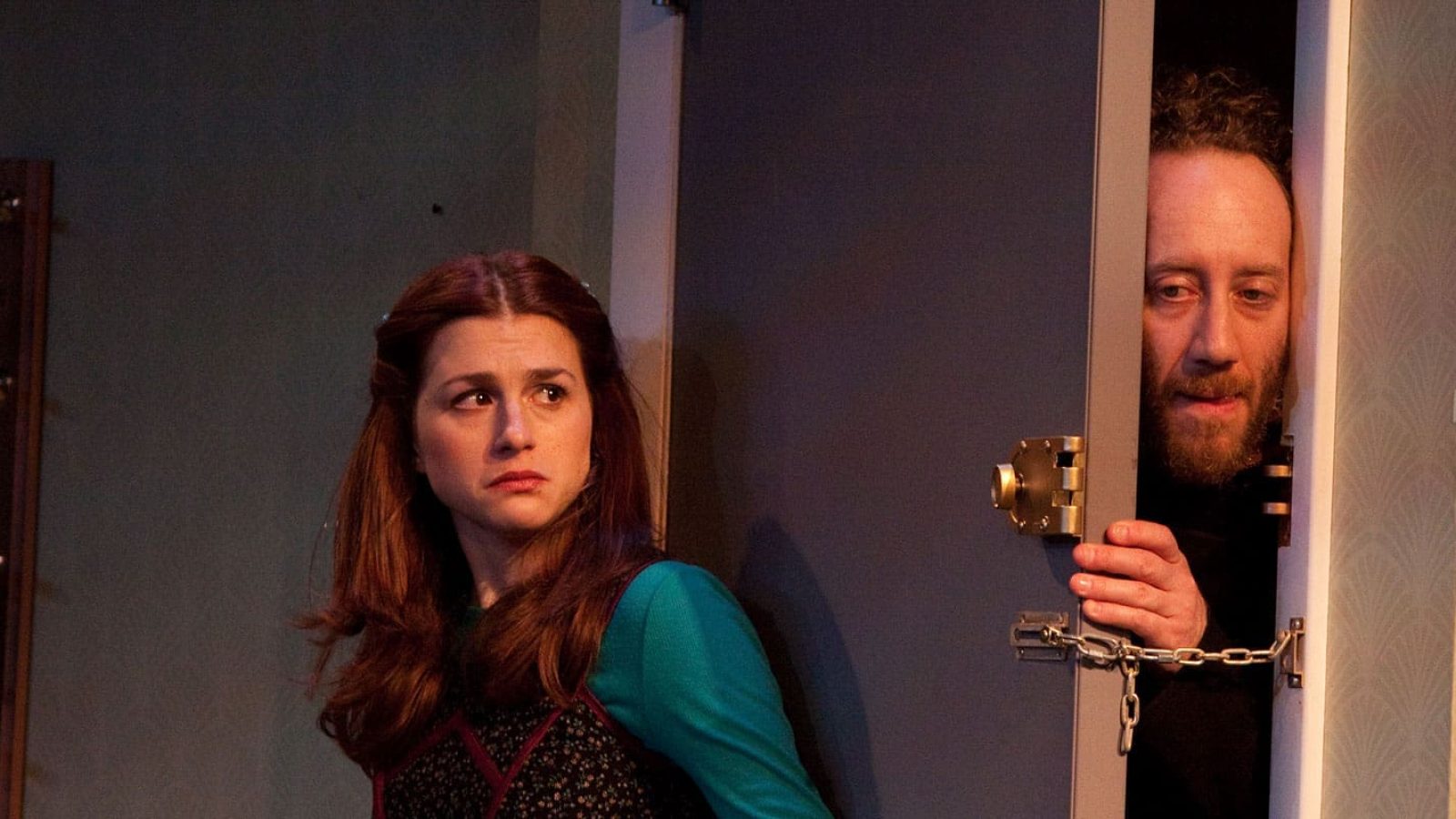 Woman looking concerned while a man hides behind a door