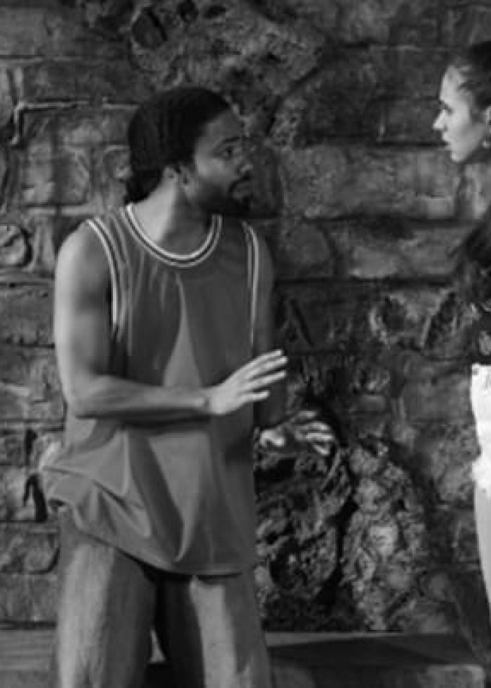 Actors in a scene from 'Tell Hector I Miss Him' in front of a brick wall.