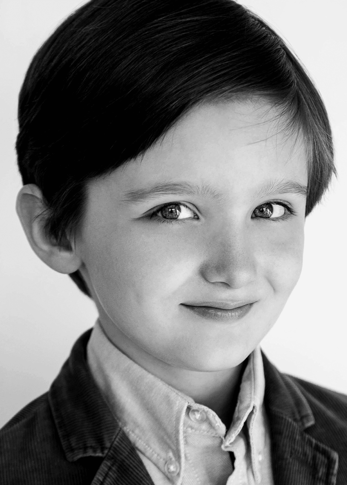 Young boy with dark hair, smiling, wearing a jacket and shirt