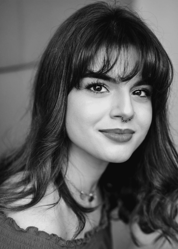 Young woman with dark hair and septum piercing smiles at the camera.