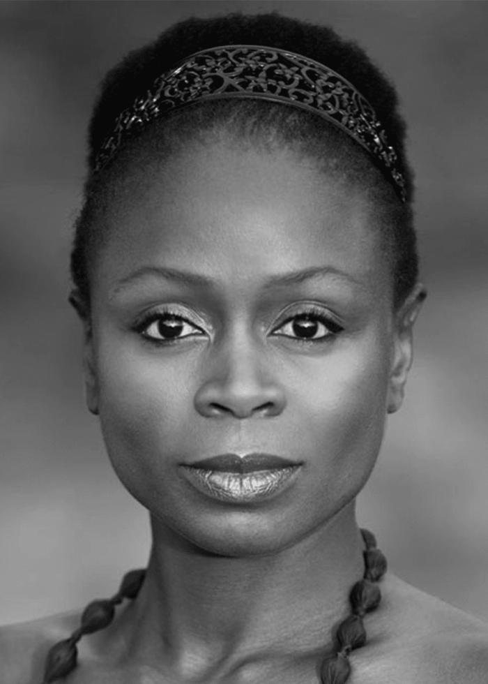 Zainab Jah in a headshot, wearing a headband and necklace, looking directly at the camera.