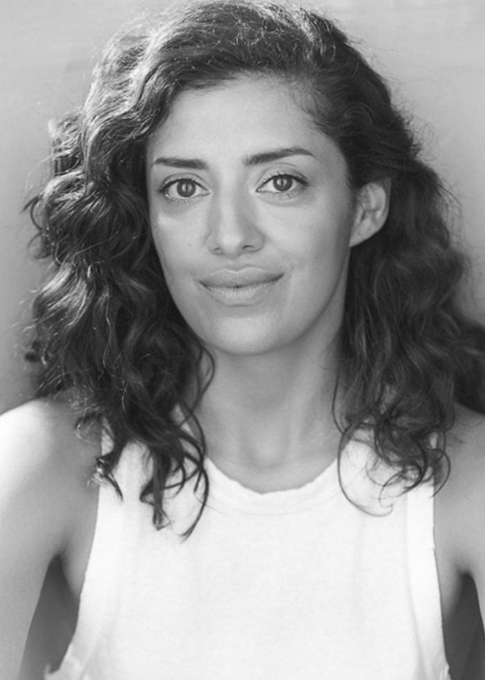 Janice Amaya, a woman with curly hair, smiles at the camera in a white tank top.