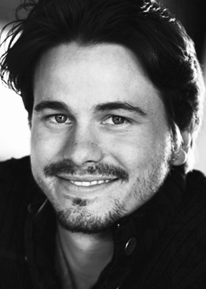 Jason Ritter smiling in a black and white portrait