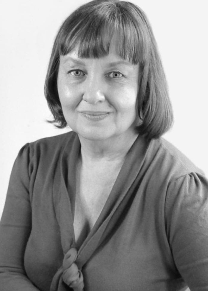 Portrait of a woman with short hair, wearing a dark top, looking at the camera.