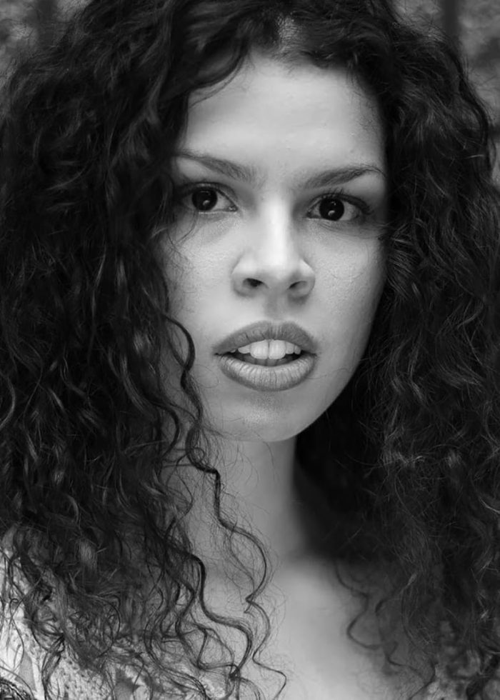 Black and white portrait of a woman with curly hair, looking directly at the camera.