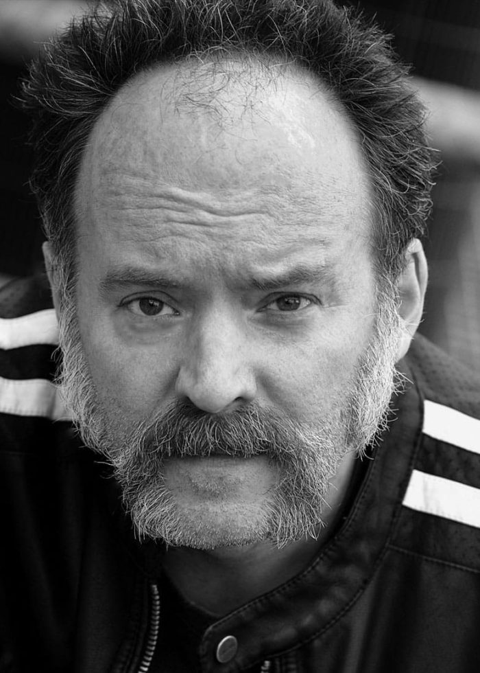 Joe Cassidy looking directly at the camera with a serious expression, wearing a jacket.