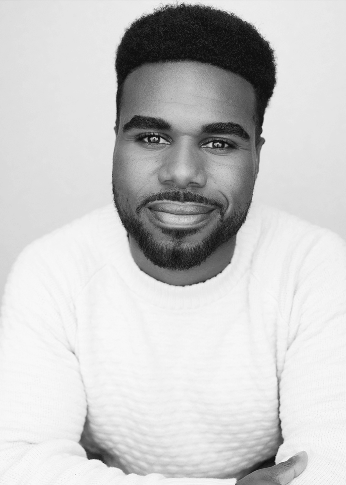 Justin Showell smiling in a black and white headshot, wearing a white sweater.