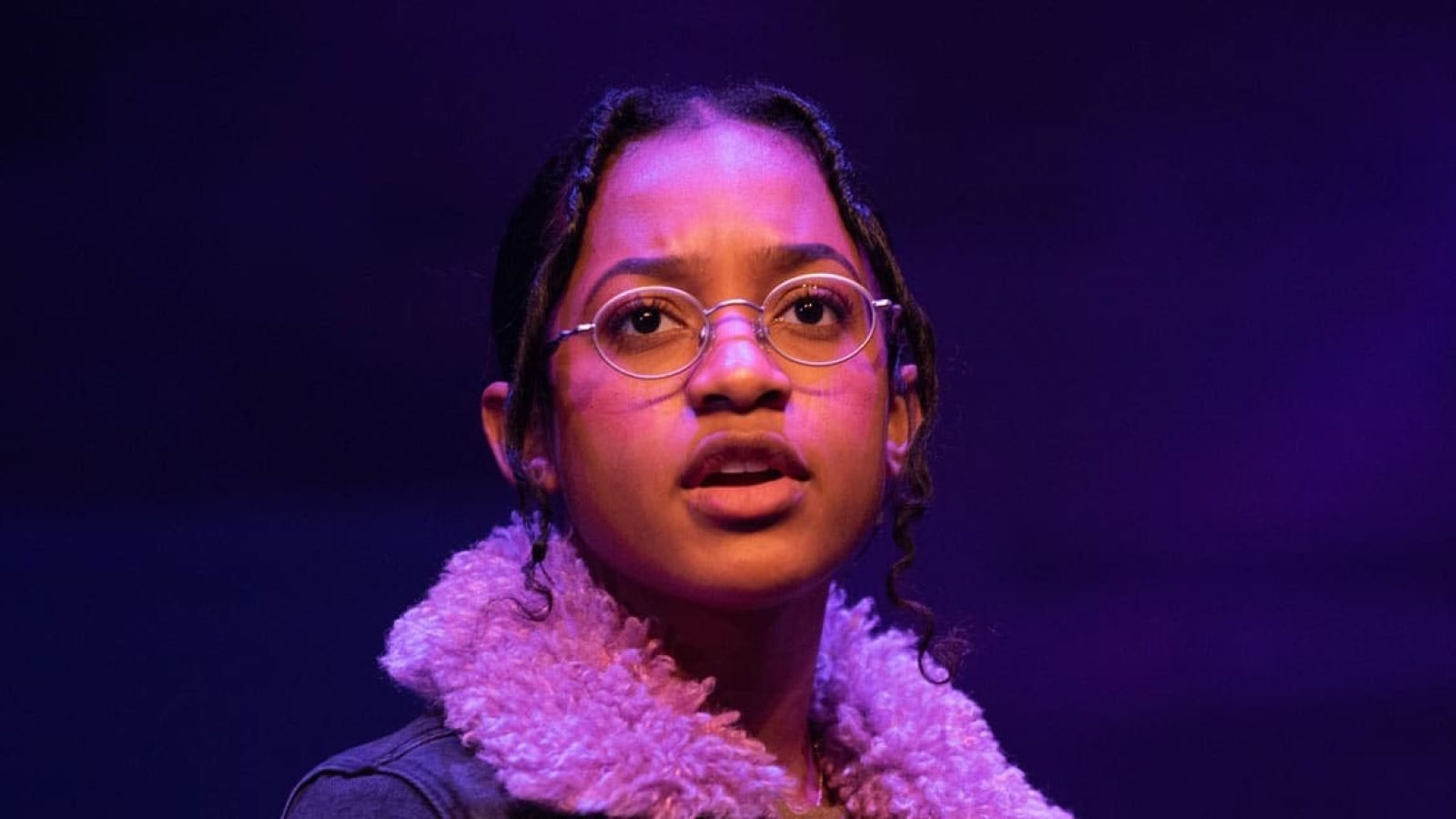 Close-up portrait of a young woman wearing glasses, looking surprised, from the play Kimberly Akimbo.
