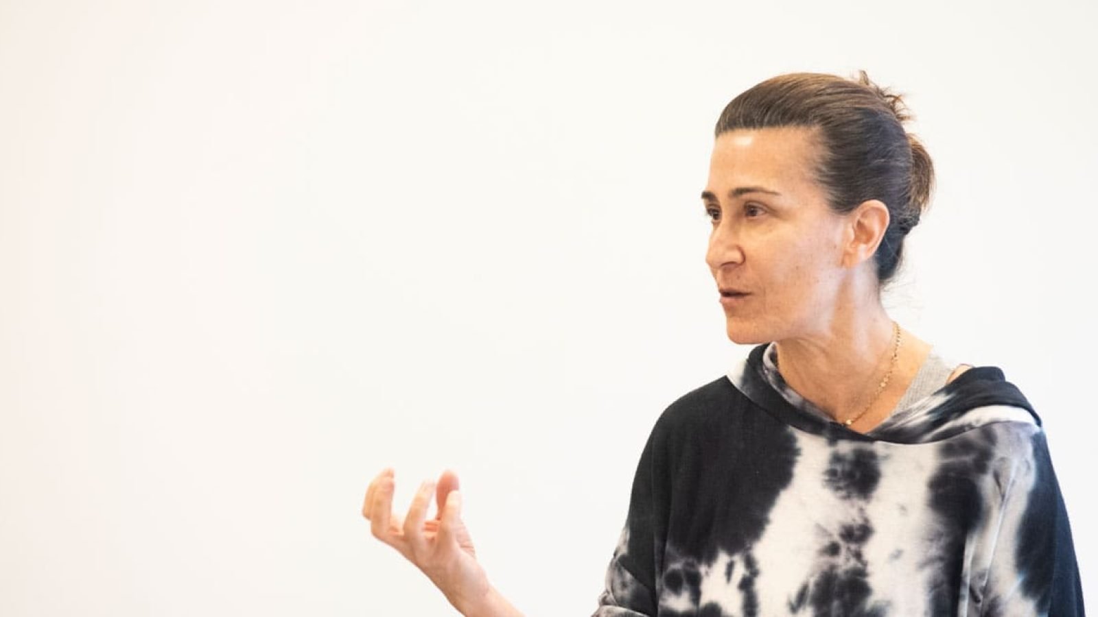 Woman speaking, wearing a tie-dye hoodie.