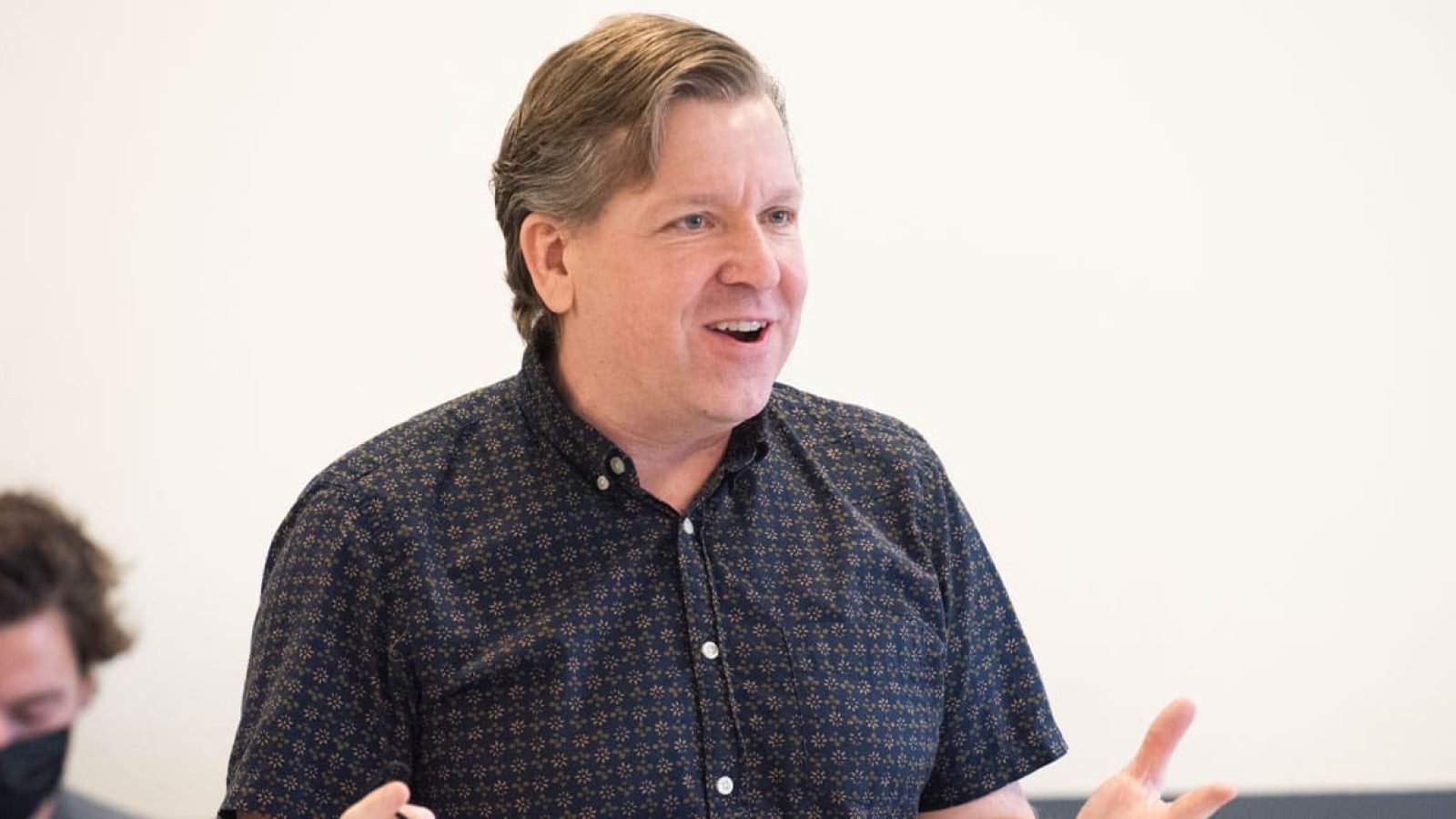 Man in patterned shirt speaking animatedly