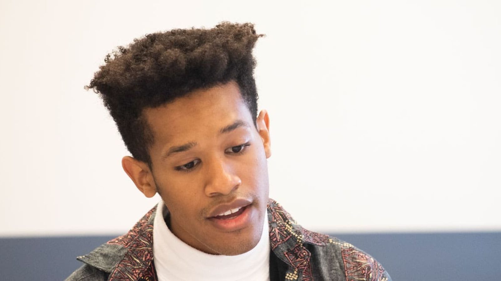Young man with short, curly hair looking down
