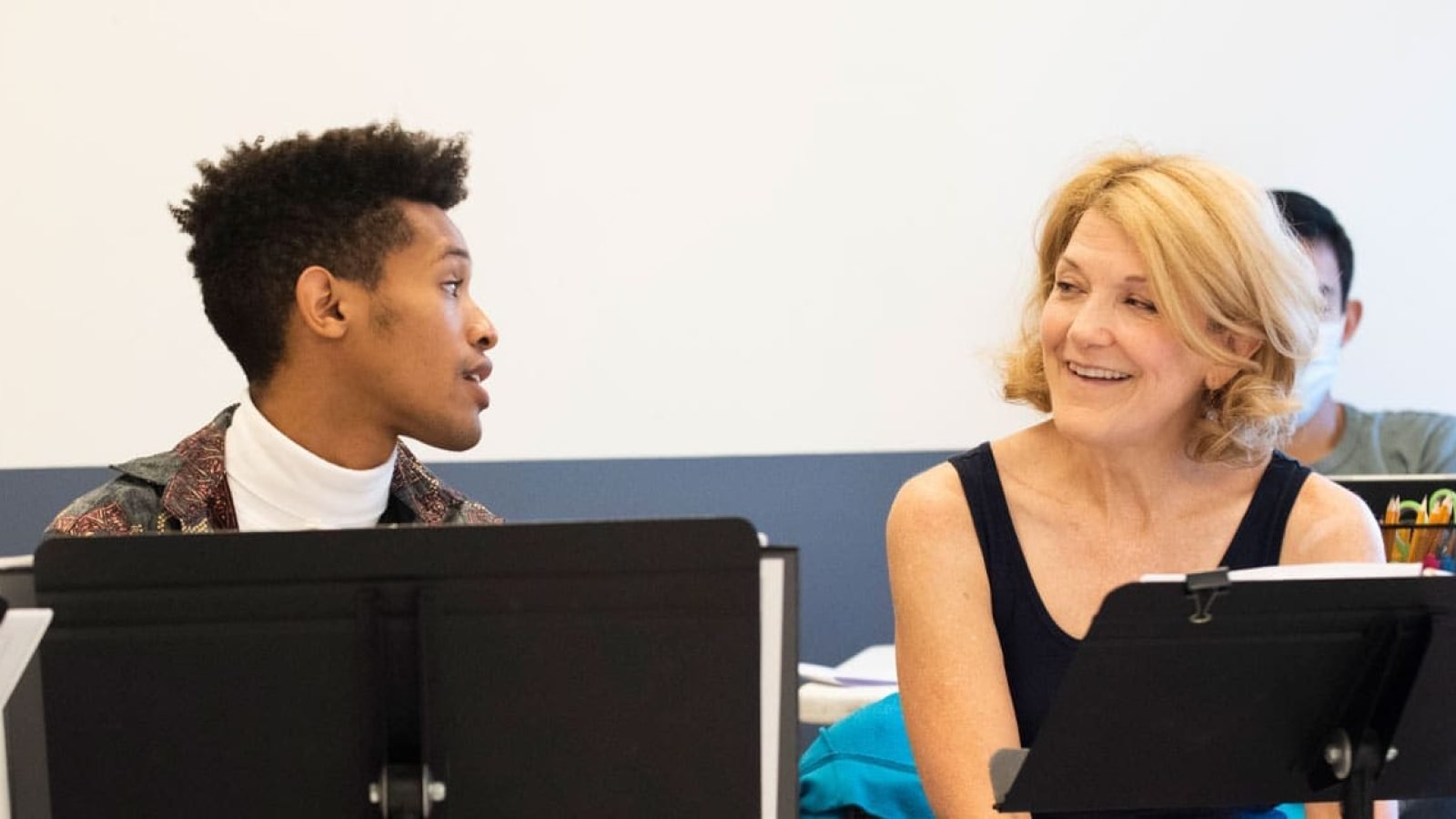 A young man and woman engage in a rehearsal, likely for a theater production like Kimberly Akimbo, each with music stands in front of them.