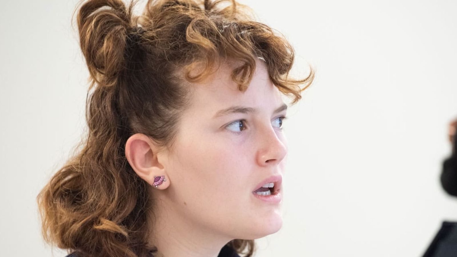 Close-up of a young woman with curly hair, looking thoughtfully to her right.
