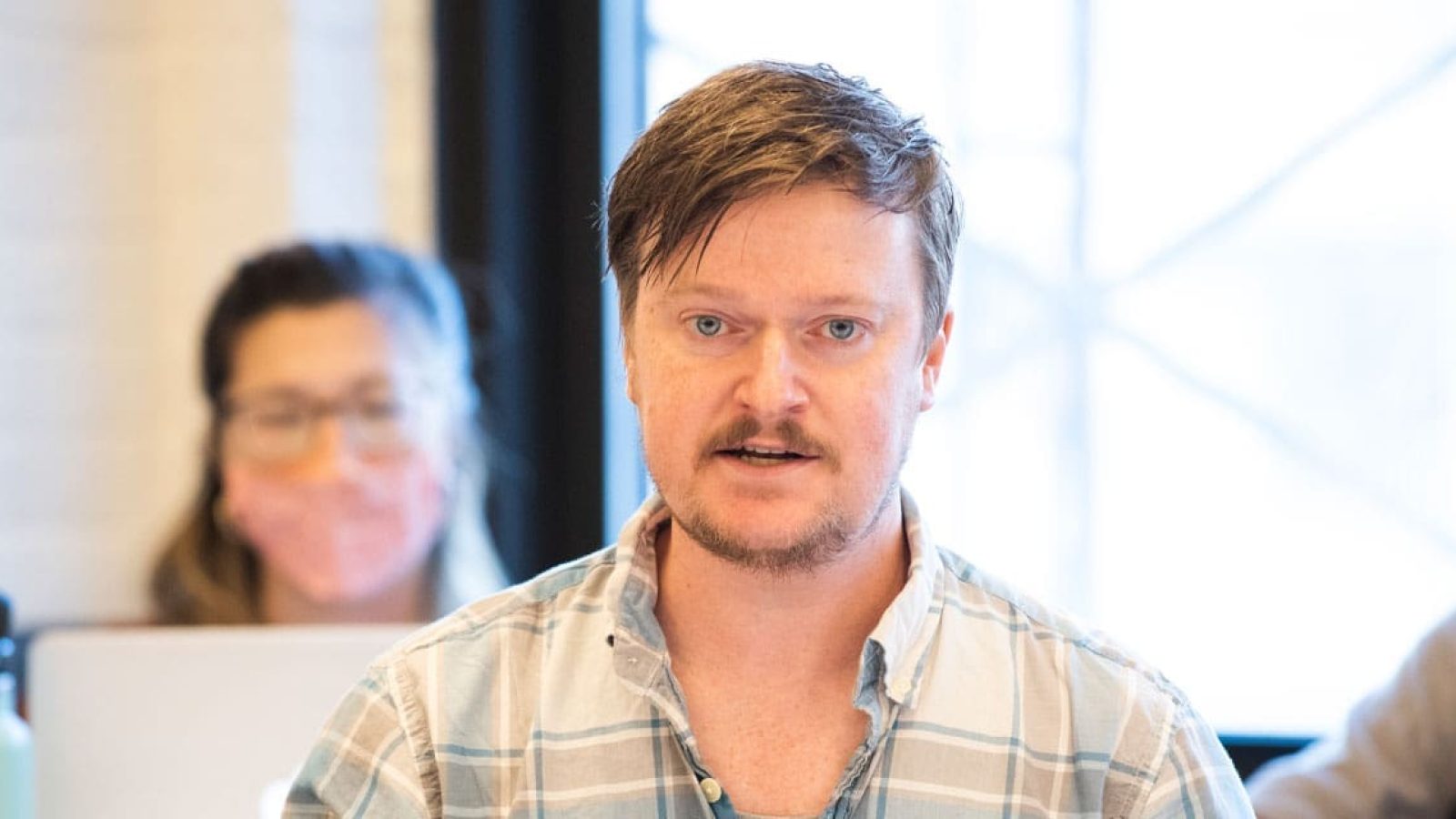 Man with light brown hair and beard speaks during a meeting.