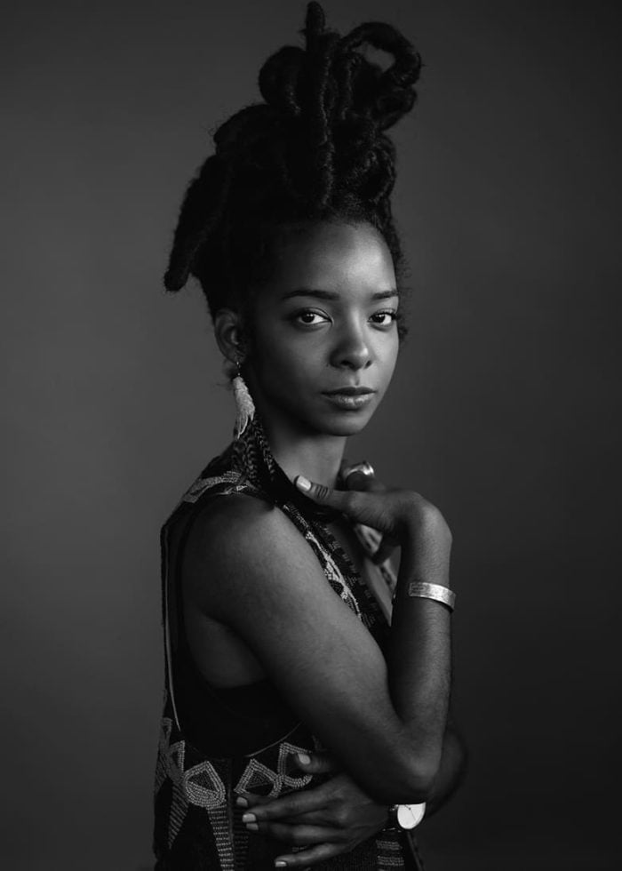 Kara Young in a striking black and white portrait. She wears a detailed vest and has dreadlocks.