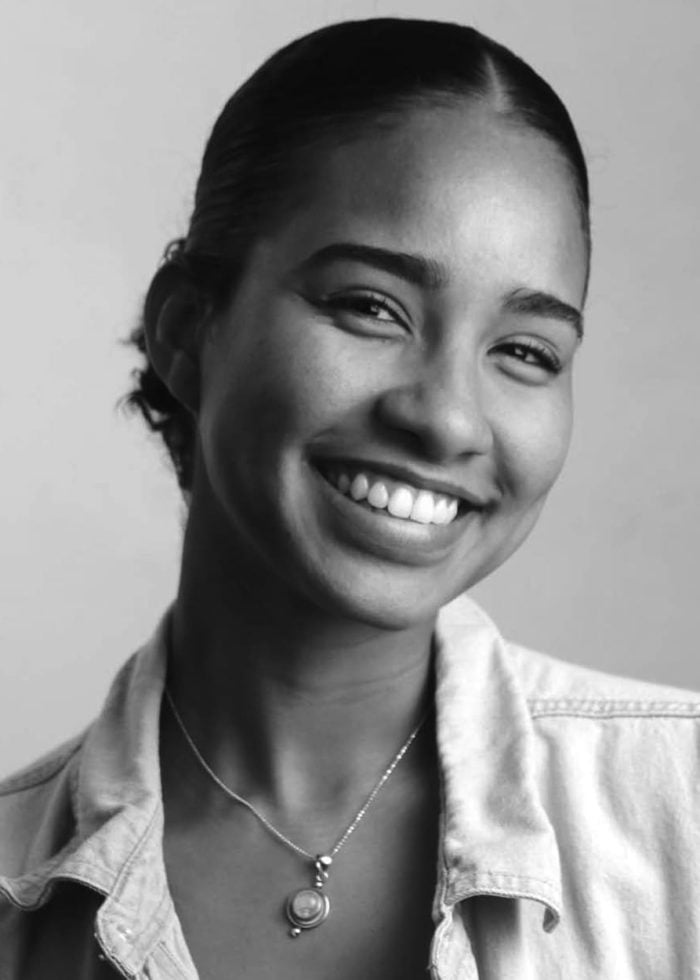 Kenya Browne smiling, wearing a denim shirt and necklace, looking at the camera.
