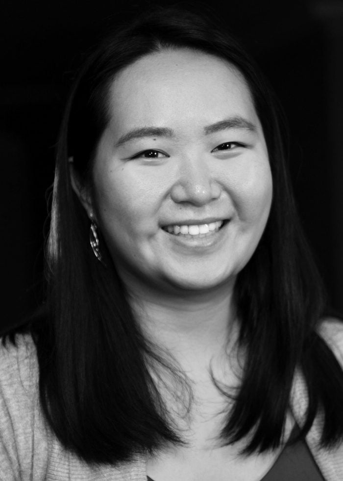 Smiling Asian woman with long dark hair, wearing earrings and a light sweater