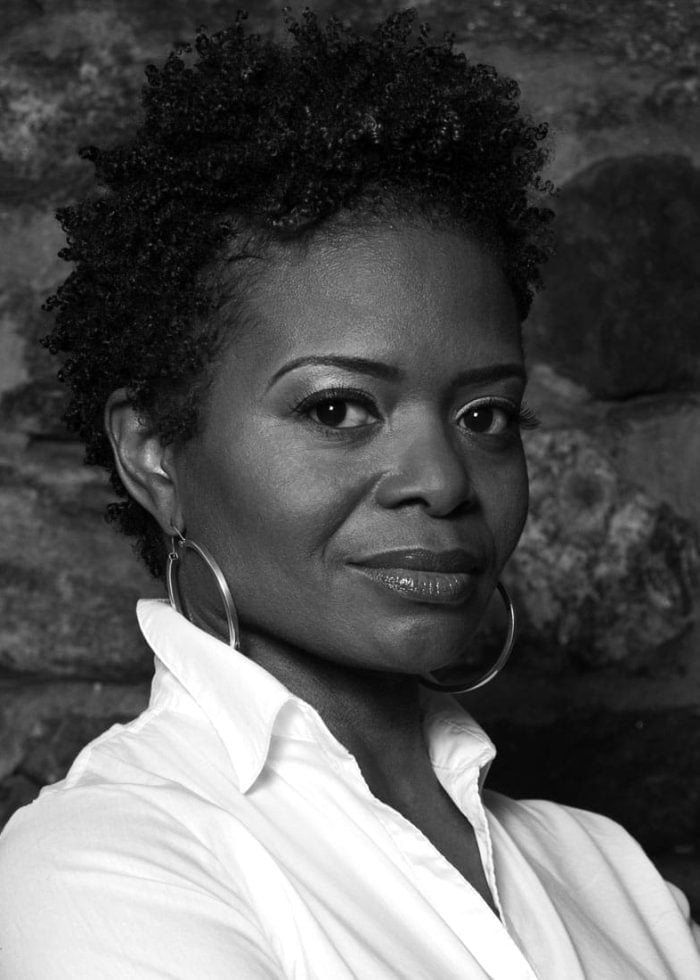 Black and white portrait of a woman with short curly hair, wearing a white shirt and hoop earrings.