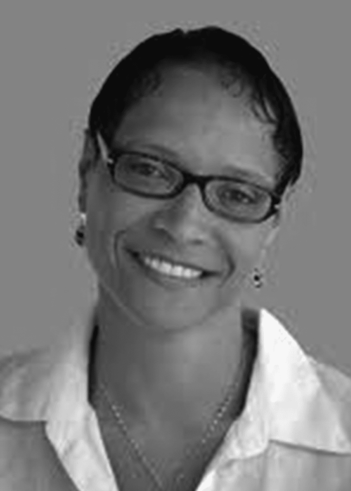 Leah C. Gardiner smiling, wearing glasses and a white shirt.