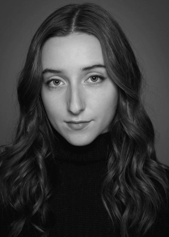 Young woman with long wavy hair in a black turtleneck looking at the camera.
