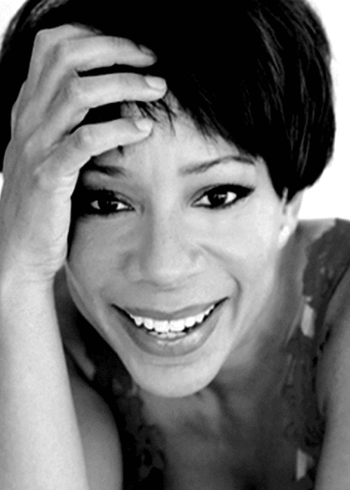 Selenis Leyva smiling, looking at the camera, with hand on head