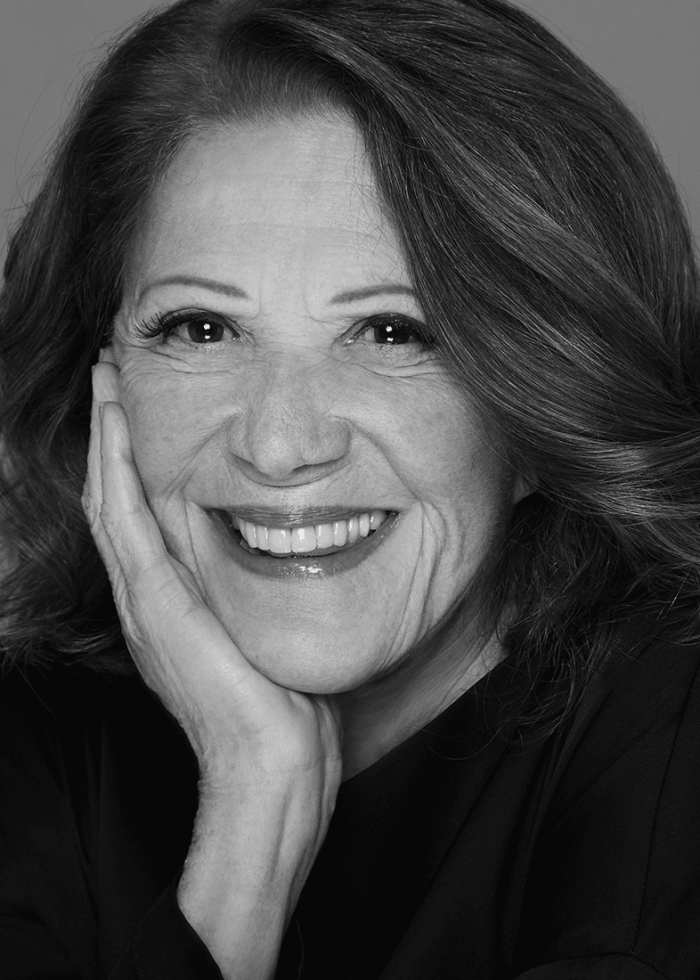 Linda Lavin smiles, resting her face on her hand, in a black and white portrait.