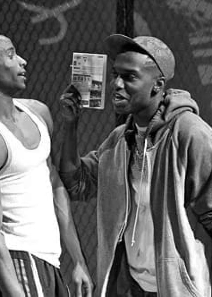 Two actors in a scene from "The Loneliness of the Long Distance Runner" play, one holding a piece of paper.