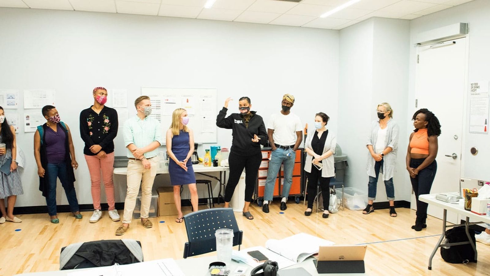 A diverse group of people wearing masks stand in a room during a meeting.
