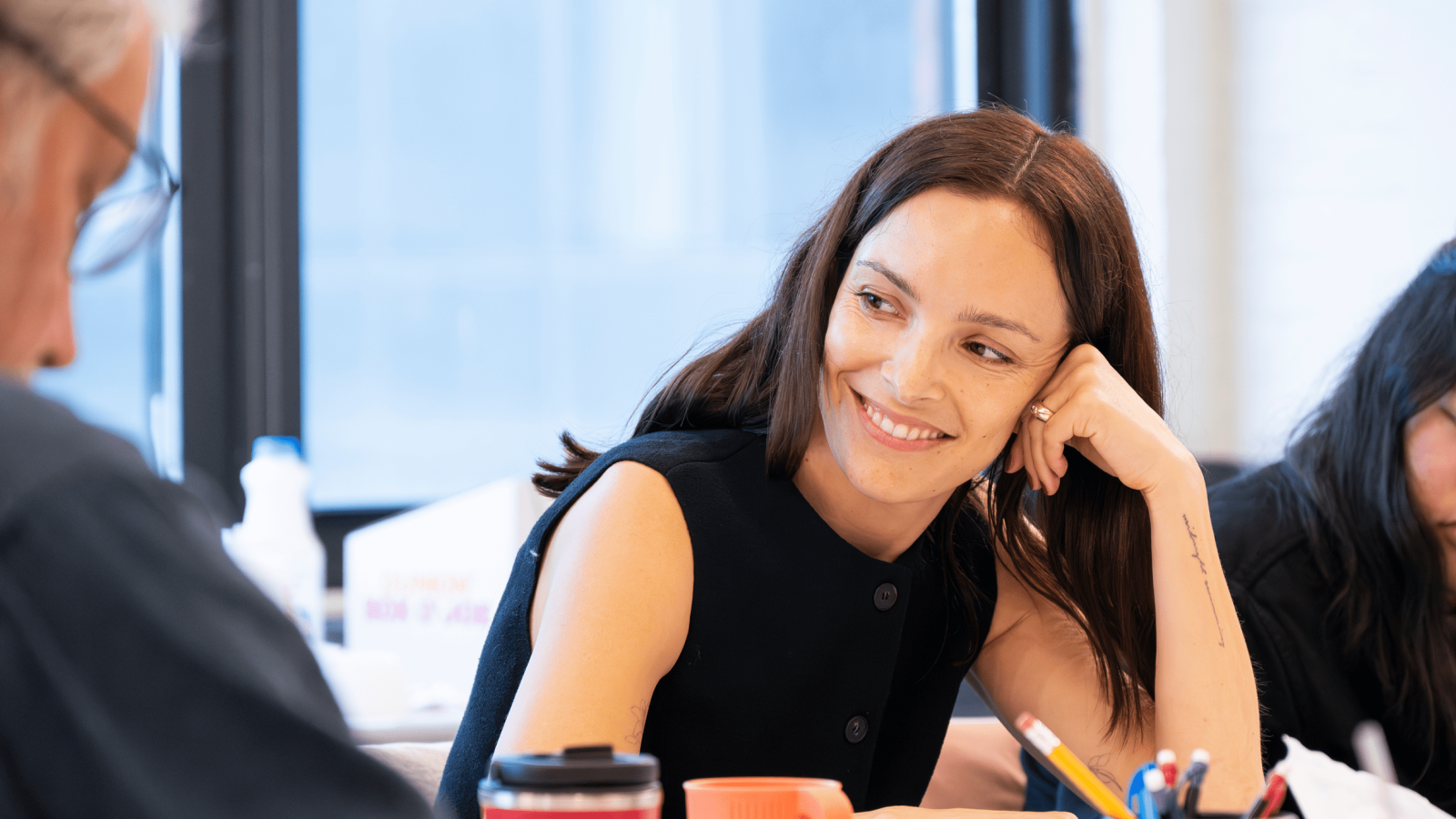 Smiling woman in a black sleeveless top, engaged in conversation.