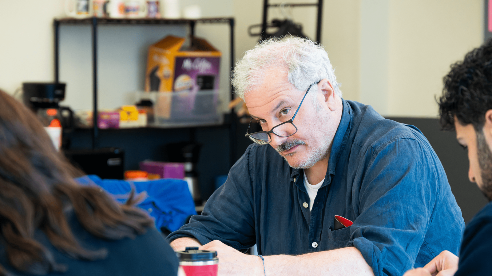 Man with glasses sits at a table, looking intently at something.