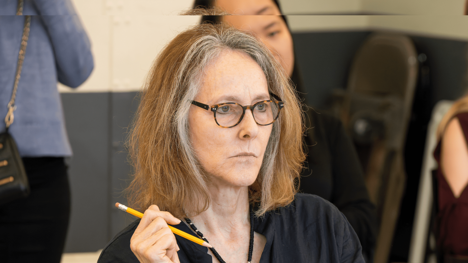 Woman with glasses thoughtfully holding a pencil