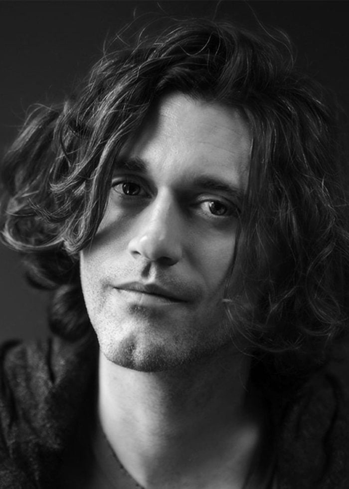 Portrait of Lucas Hnath with long, wavy hair in black and white
