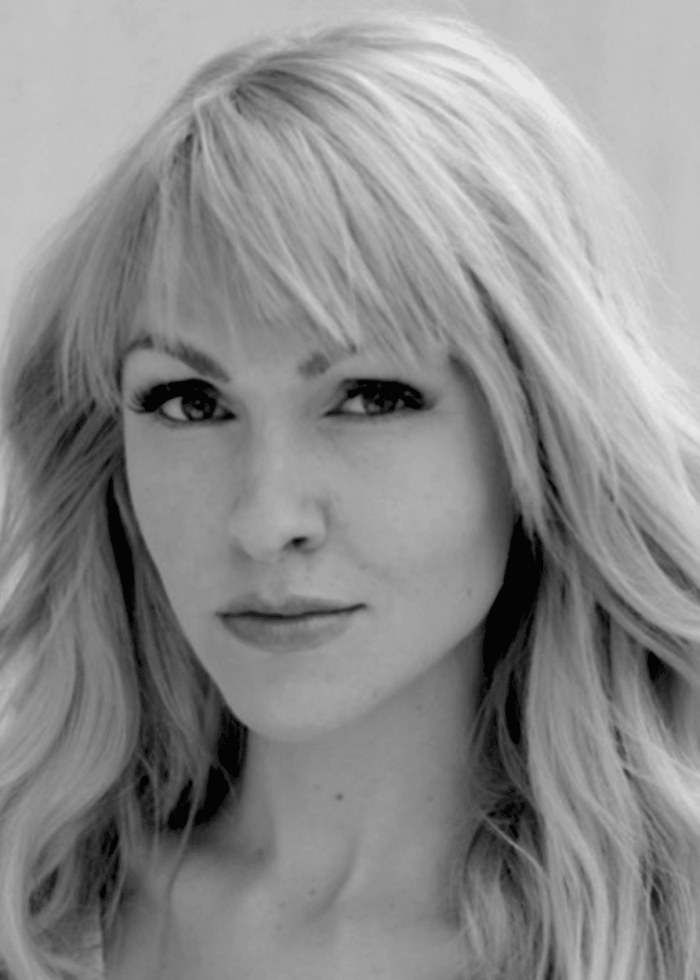 Blonde woman with long wavy hair and bangs, looking directly at the camera.