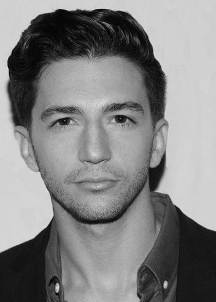 John Magaro in a headshot, wearing a blazer and button-down shirt.