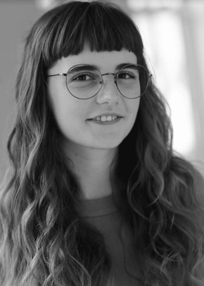 Portrait of a young woman with wavy hair, round glasses, and a friendly smile