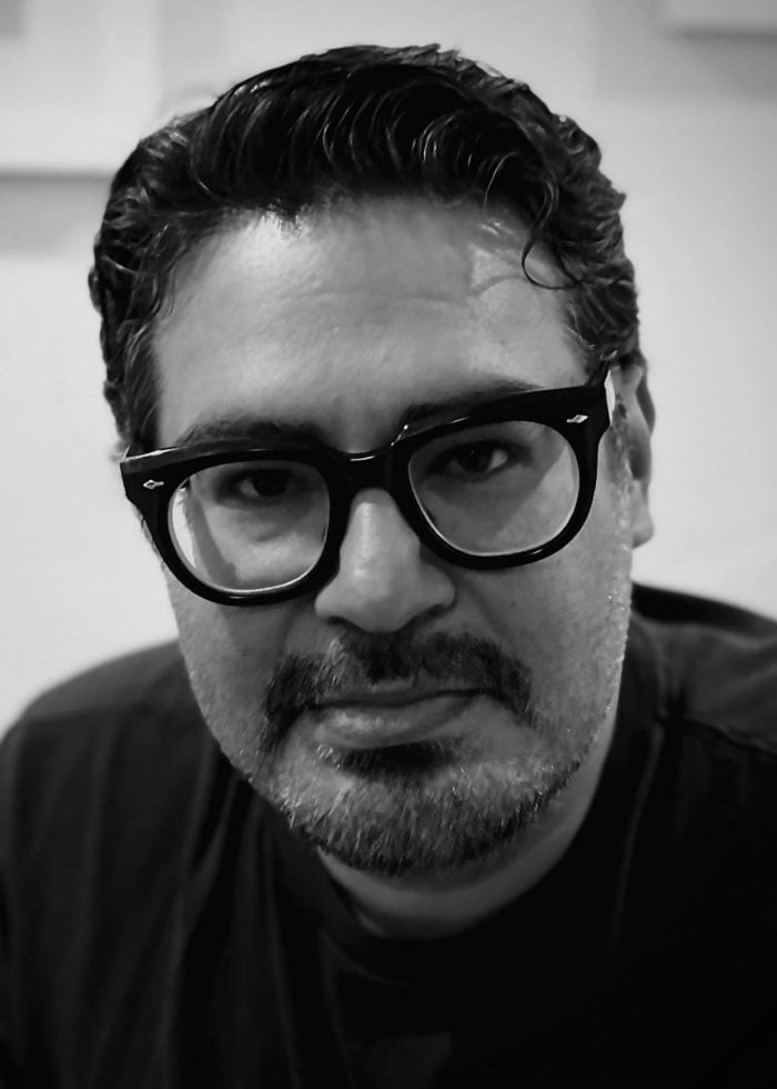 Mando Alvarado wearing glasses, looking at the camera in black and white.