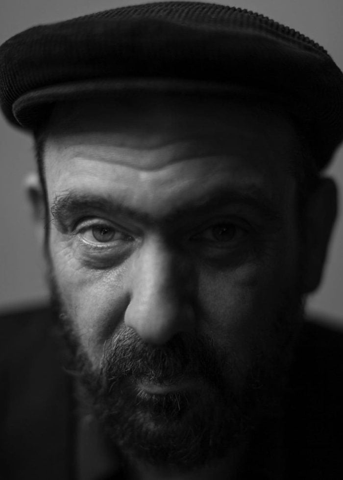 Close-up portrait of Mark Eitzel wearing a hat, in black and white.