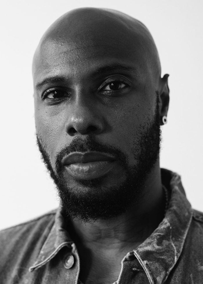 Marquise Vilsón, a Black man with a bald head and beard, looks directly at the camera in a black and white portrait.