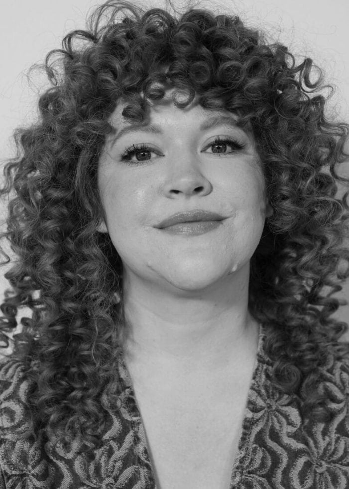 Black and white portrait of actress Mary Wiseman with curly hair.