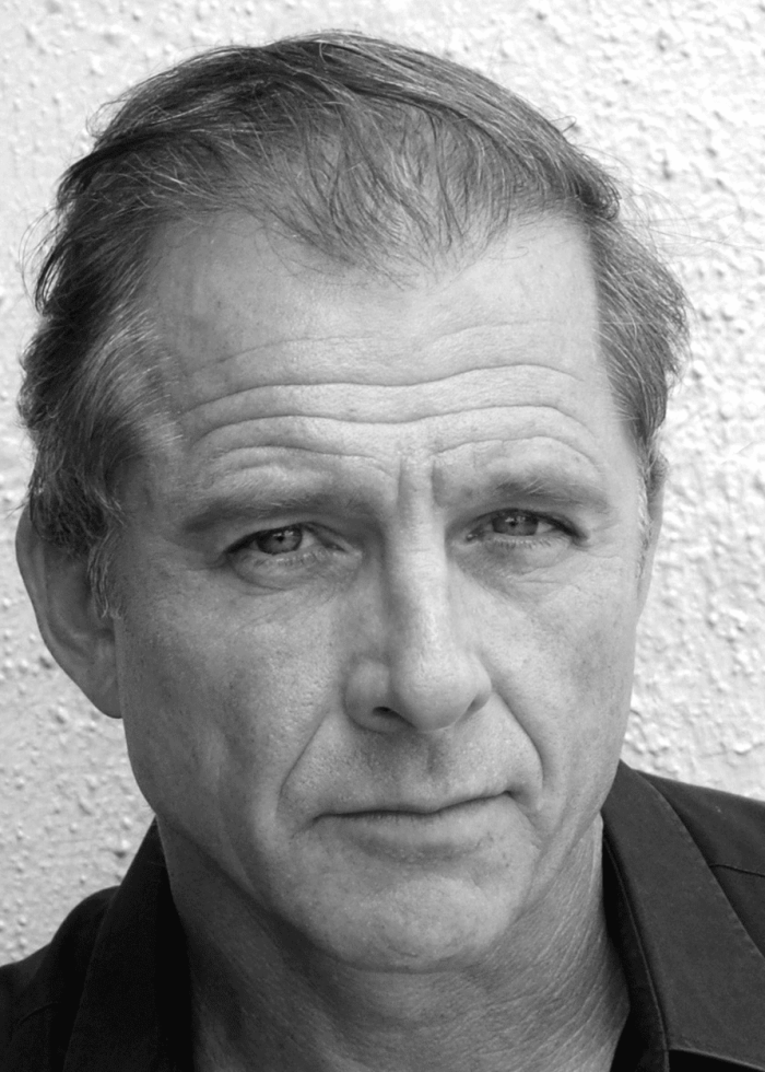 Maxwell-Caulfield-8×10-i Maxwell Caulfield in a close-up black and white headshot, looking directly at the camera.